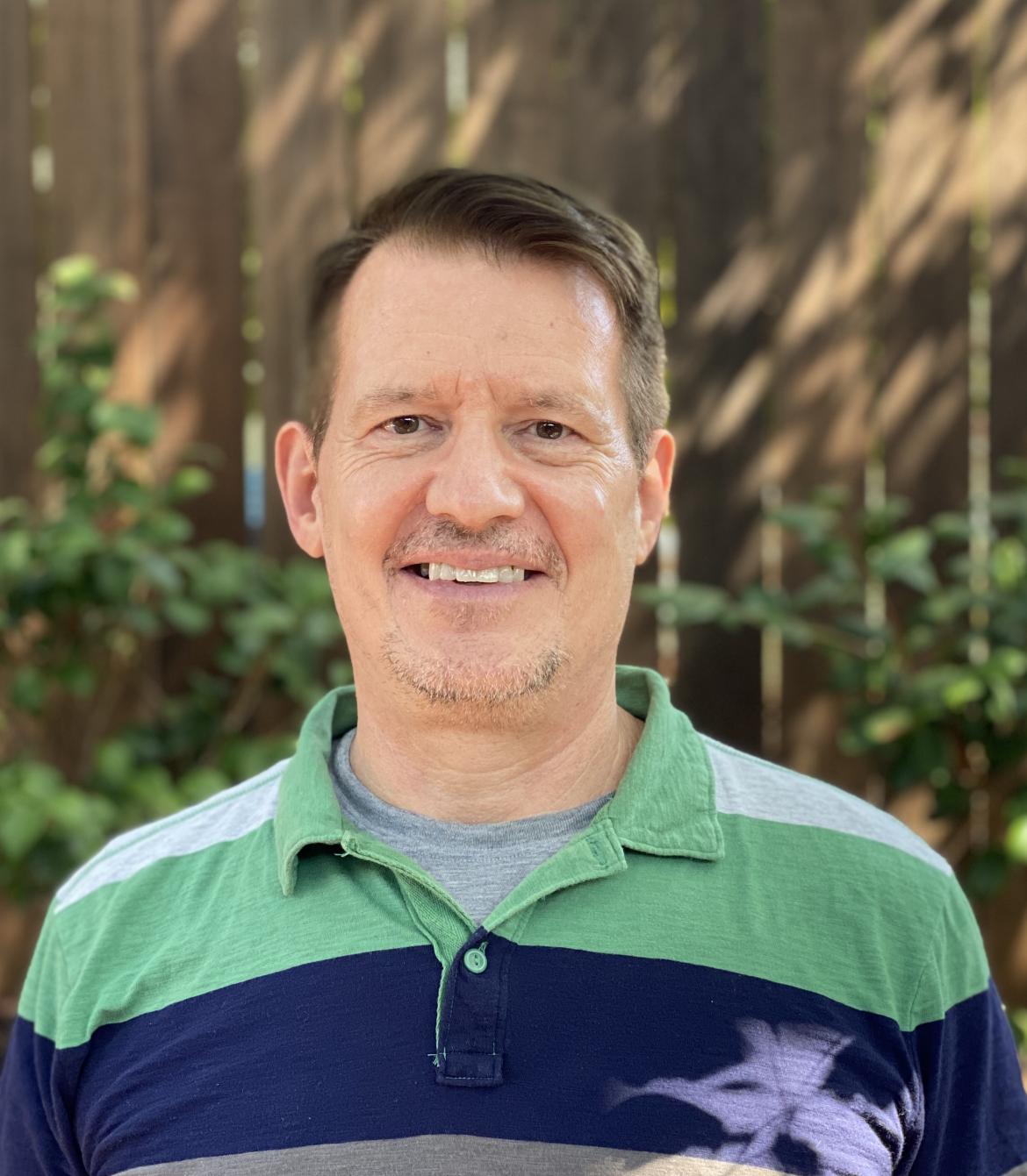 Psychiatrist Steve Sager wearing a green and blue striped shirt and smiling at the camera