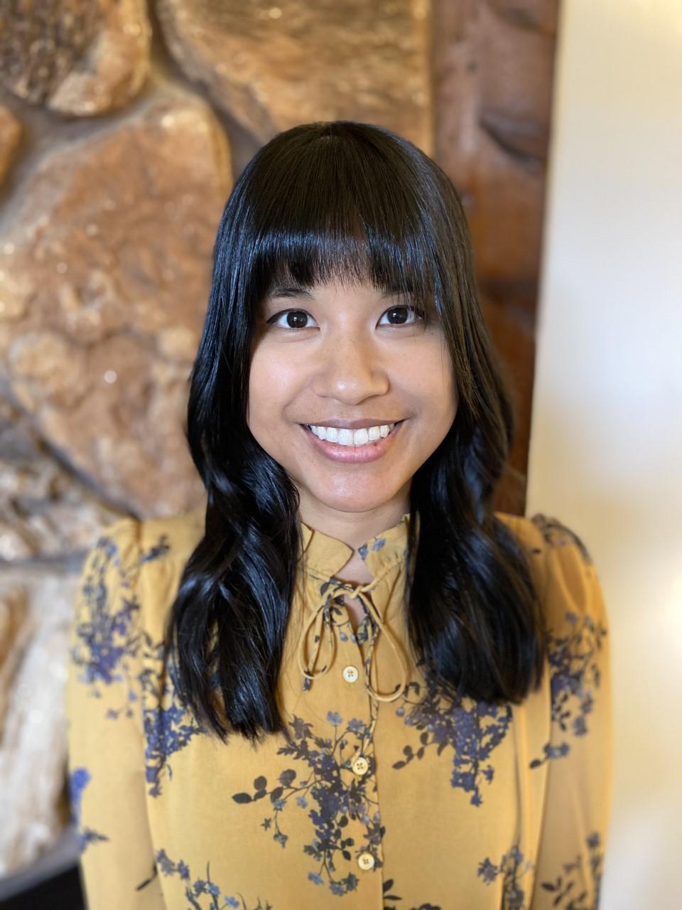 Therapist Diane Gallo smiling at the camera wearing a yellow blouse with purple flowers in front of a rock wall 