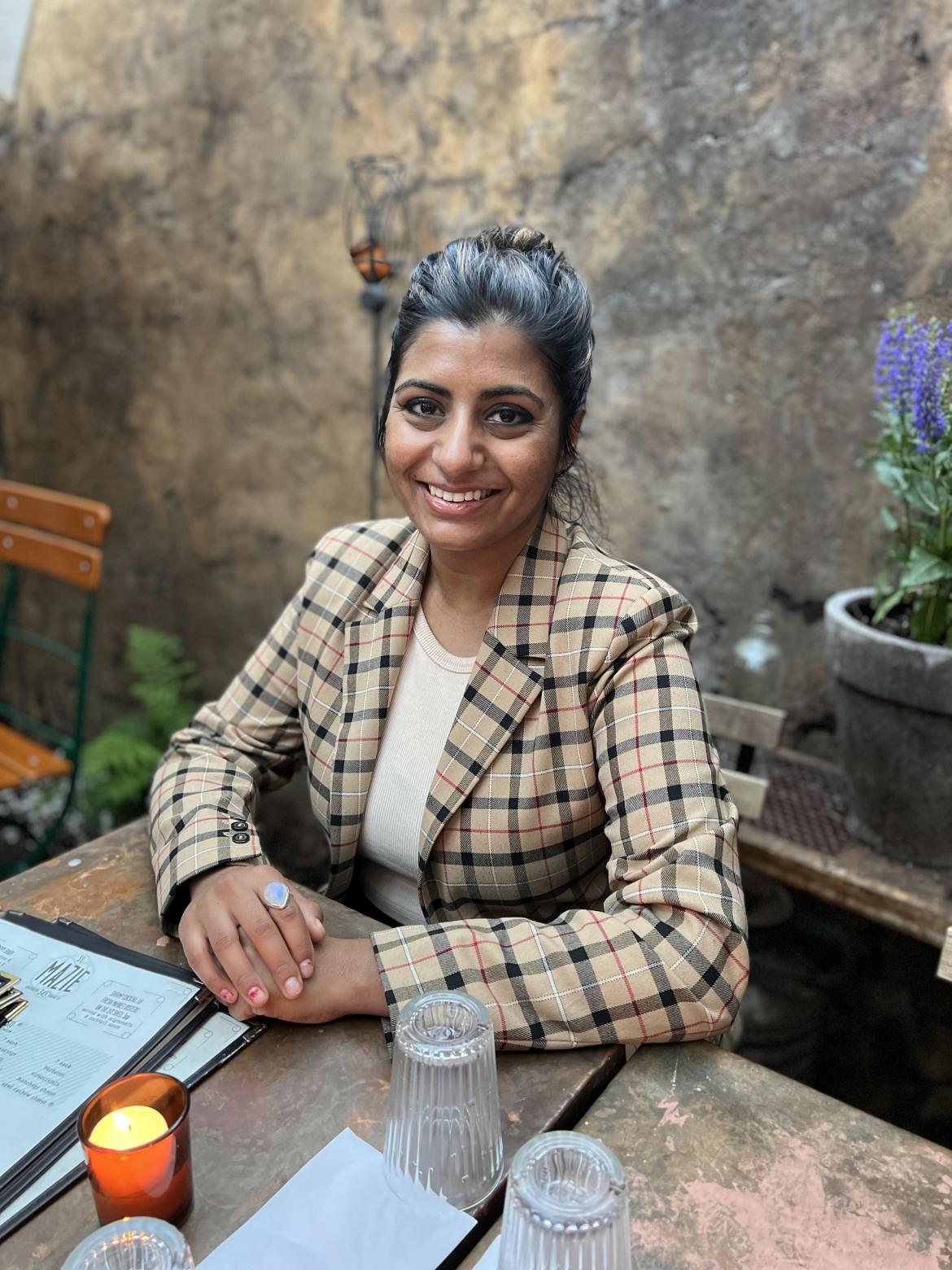 Psychiatrist Anjali Varigonda wearing a plaid blazer smiling at the camera sitting at a table 