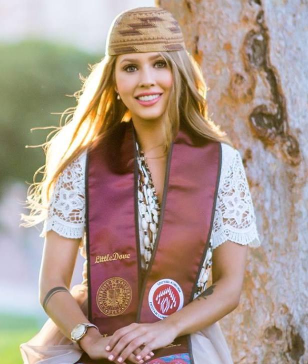 Doctoral intern LittleDove Rey smiling at the camera wearing a graduation sash and a beaded hat in front of a tree
