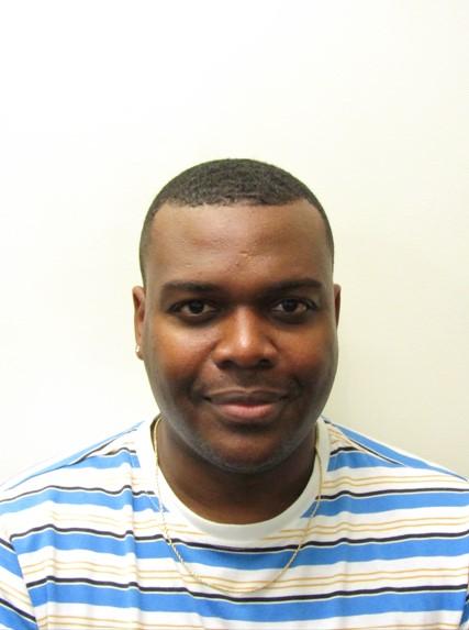 Clinical Coordinator Anthony Chambers wearing a blue, white, and yellow striped shirt smiling at the camera in front of a white background