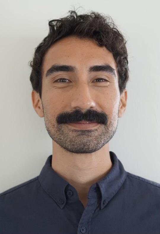 Trainee Michael Olivares smiling at the camera wearing a navy blue button up shirt in front of a white background