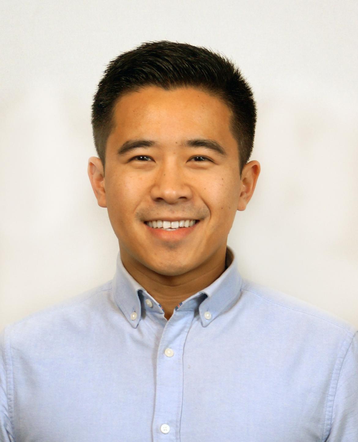 Therapist Xiaoming Hu smiling at the camera wearing a blue button up shirt in front of a white background