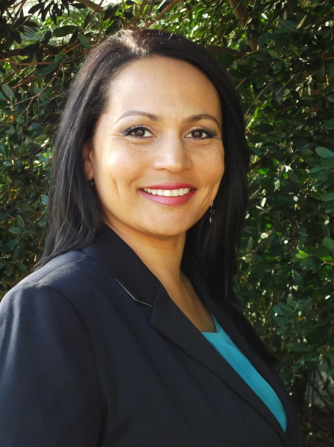 Therapist Gina Garrett wearing a blue blazer and a light blue shirt underneath smiling in front of a foliage background 