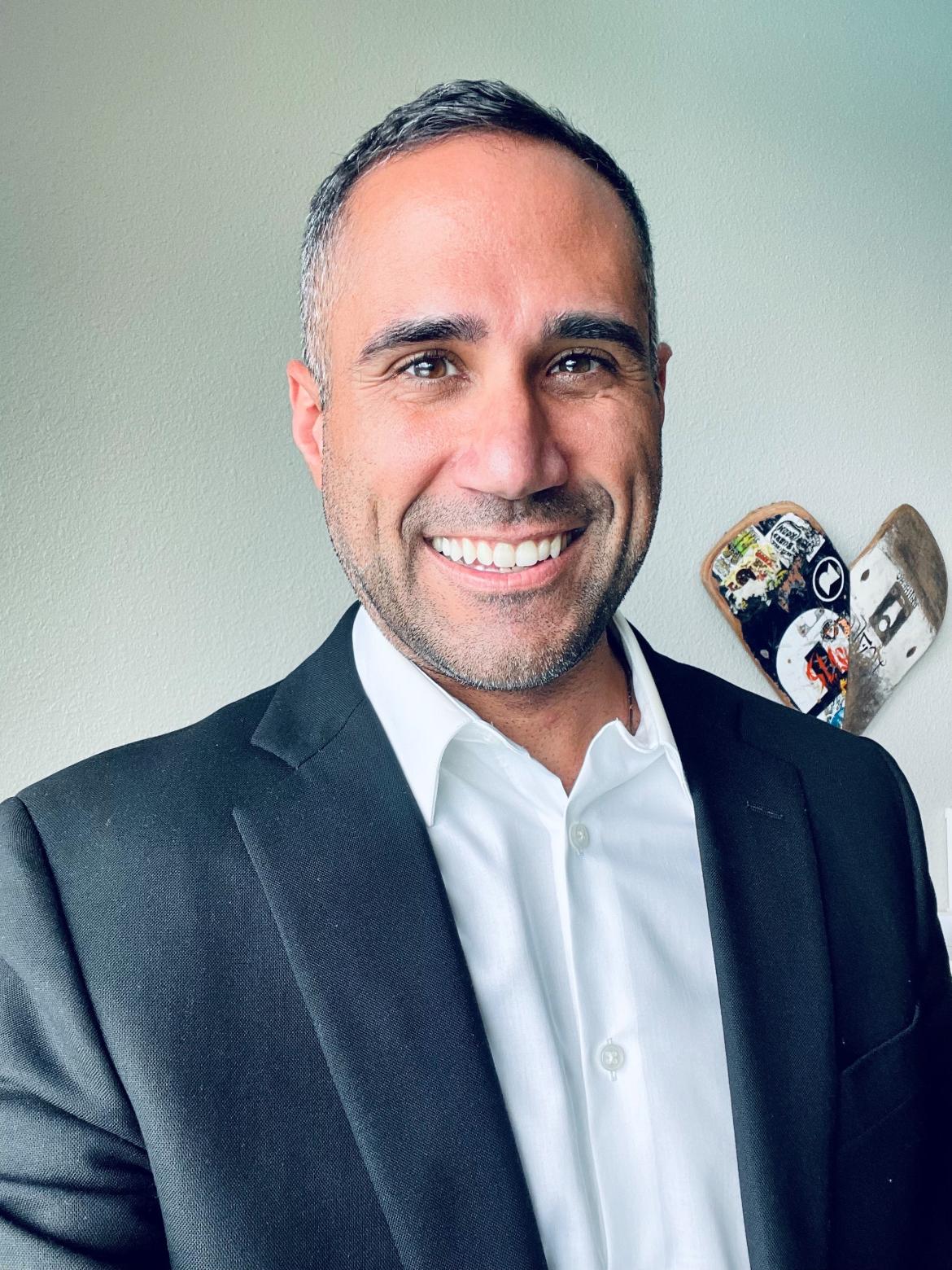 Therapist Gregory Matos wearing a grey blazer over a white button up shirt smiling at the camera