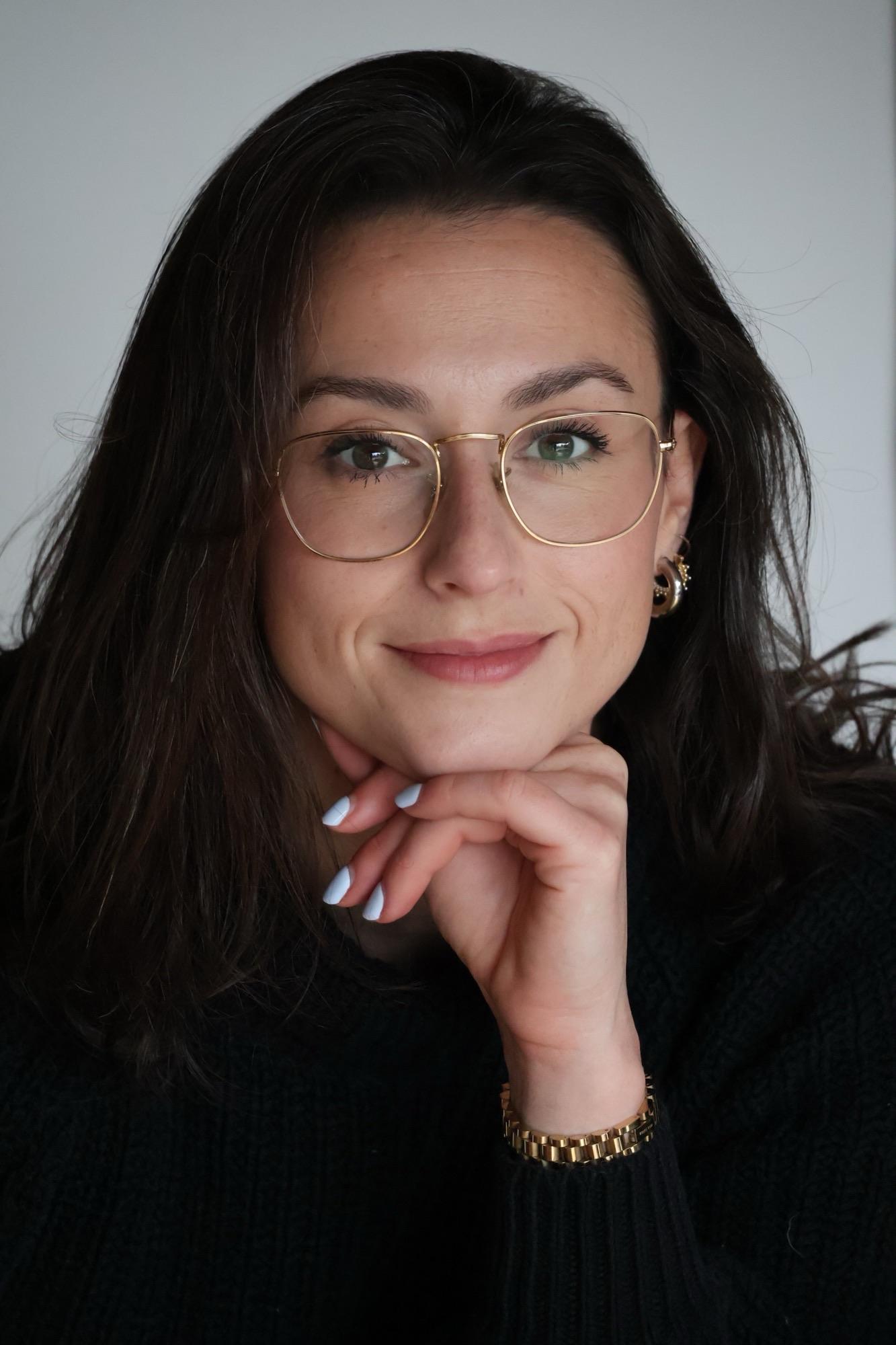 Therapist Melanie Spiegel wearing a black long sleeved shirt smiling at the camera with her head resting on her hand