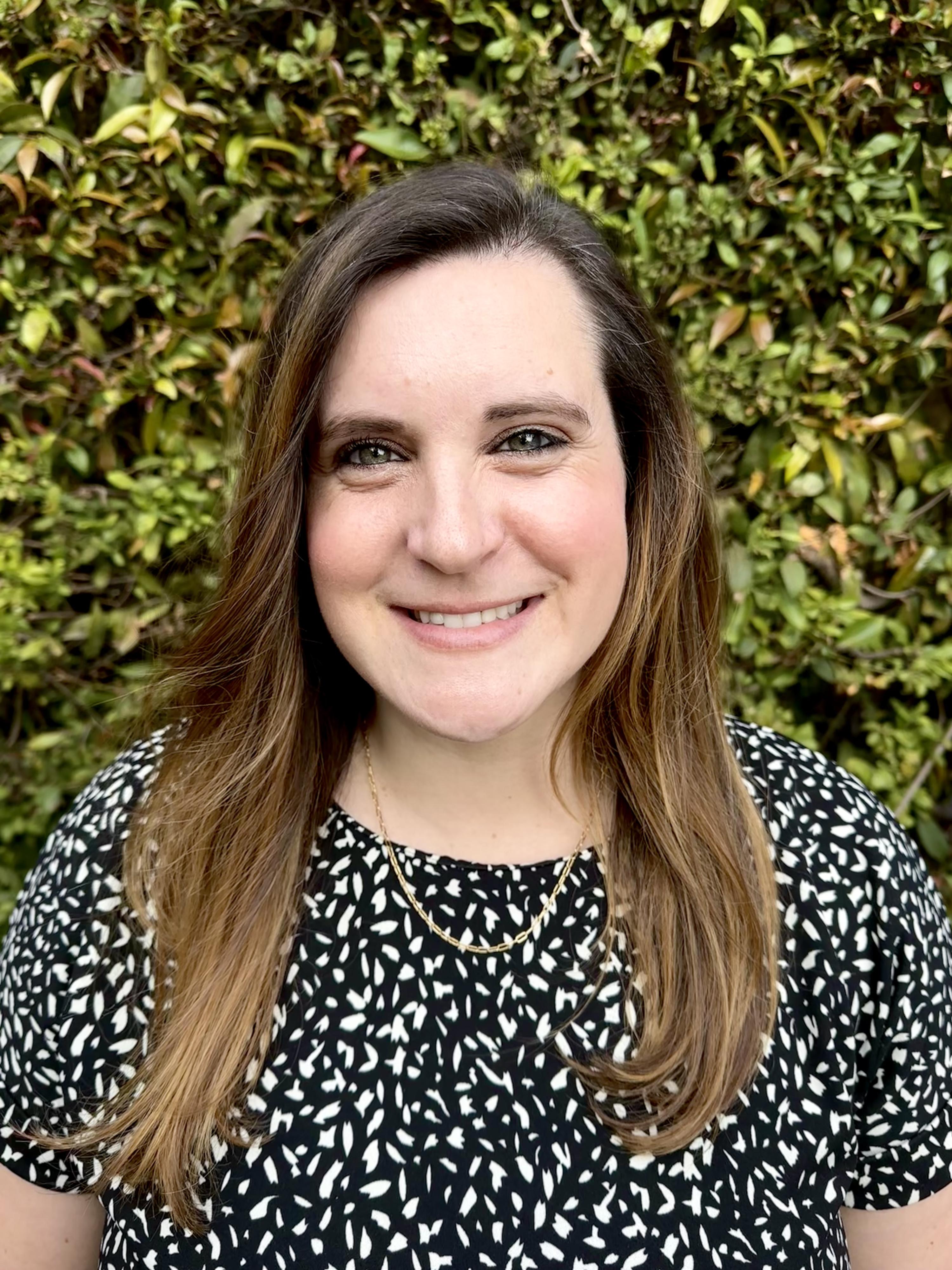 Therapist Morgan Sorenson wearing a black and white shirt smiling at the camera in front of a floral background