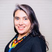 Therapist Elizabeth Hernandez smiling at the camera wearing a black blazer and colorful necklace with a white background