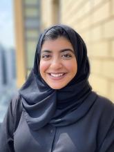 Postdoctoral Fellow Maryam Saleem smiling at the camera wearing a black hijab and black long sleeve shirt 