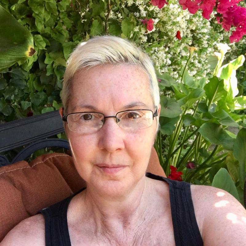 Therapist Diana Chappelear smiling at the camera wearing a black top with green foliage in the background