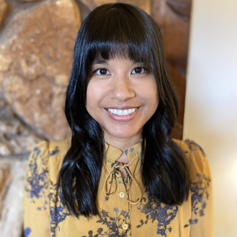 Therapist Diane Gallo smiling at the camera wearing a yellow blouse with purple flowers in front of a rock wall