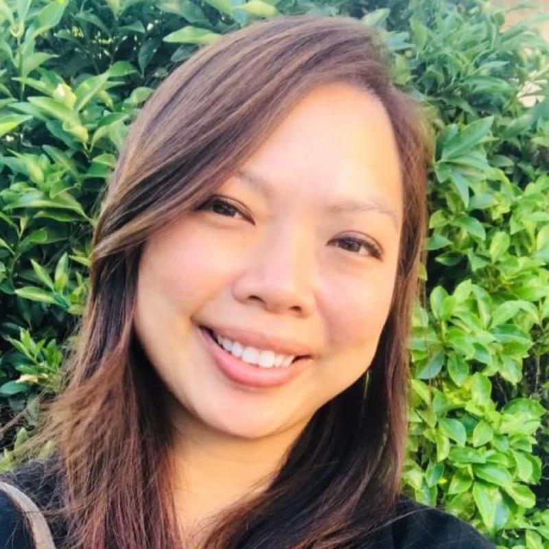 Therapist Shannen Vong wearing a black shirt smiling at the camera with green foliage in the background