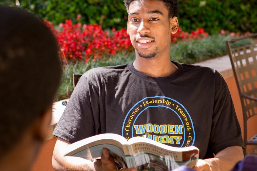student wearing a Wooden Academy t-shirt studies at an outdoor table near Bruin Cafe