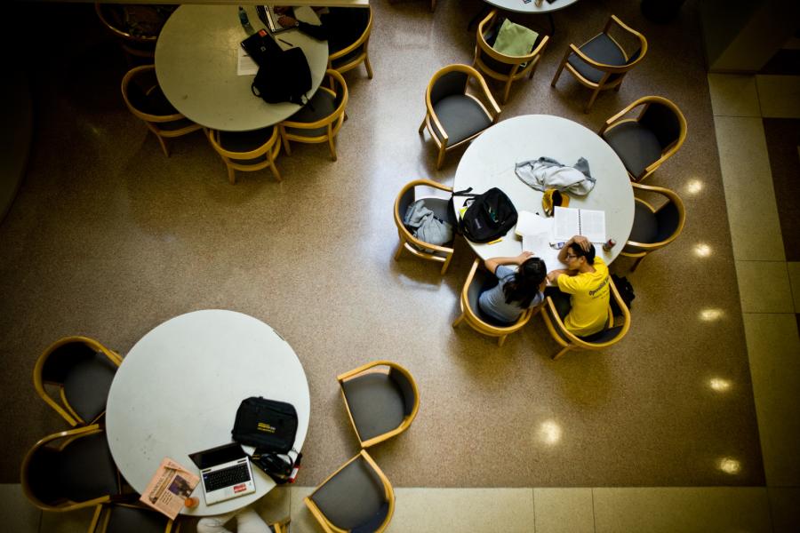 three round tables in a room with chairs around them, two students are sitting near each other at one of the tables